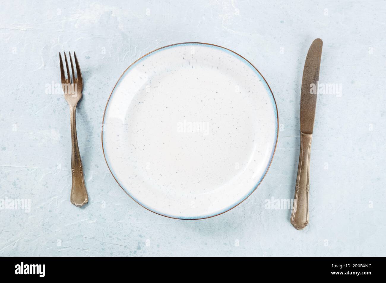 Un piatto bianco vuoto con un bordo blu, con una forchetta e un coltello, piatto sopra la testa sparato su uno sfondo ardesia, il concetto di cena Foto Stock