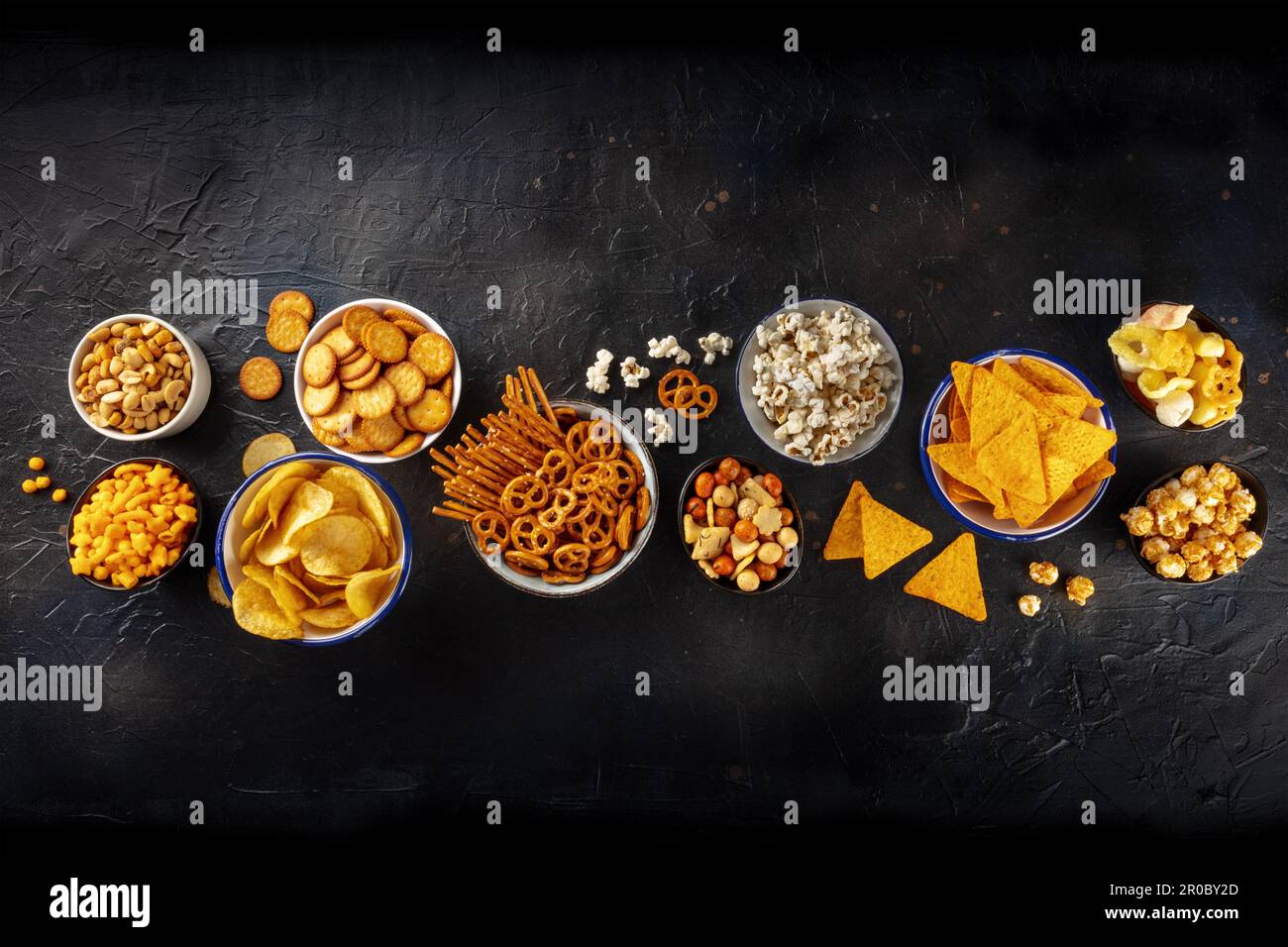 Spuntini salati, mix per feste. Un assortimento di antipasti croccanti, sparati dall'alto su sfondo nero con spazio per le copie. Patatine e tortilla, cracker Foto Stock
