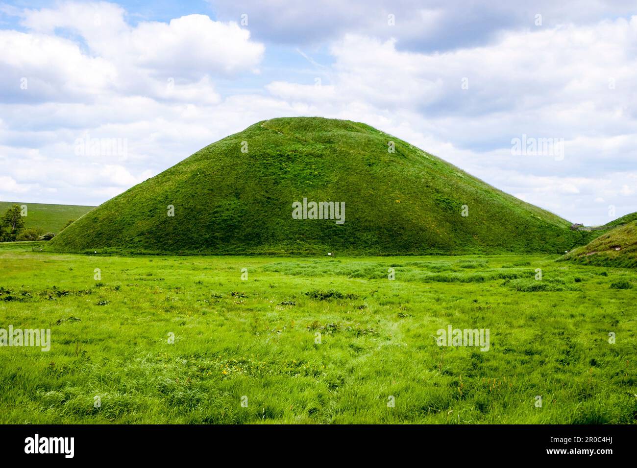 Silbury Hill, Wiltshire, Inghilterra. Un tumulo di terra neolitico, scopo sconosciuto, costruito 2400 AC. Piano terra vista estate con cielo blu nuvoloso. Foto Stock