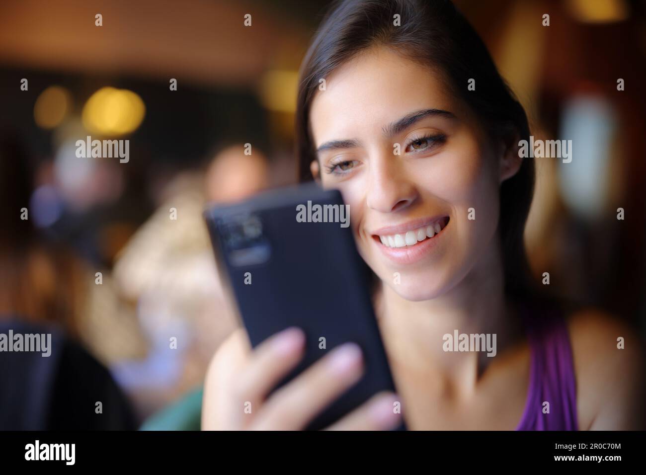 Donna felice in un ristorante che usa lo smartphone e sorridente Foto Stock