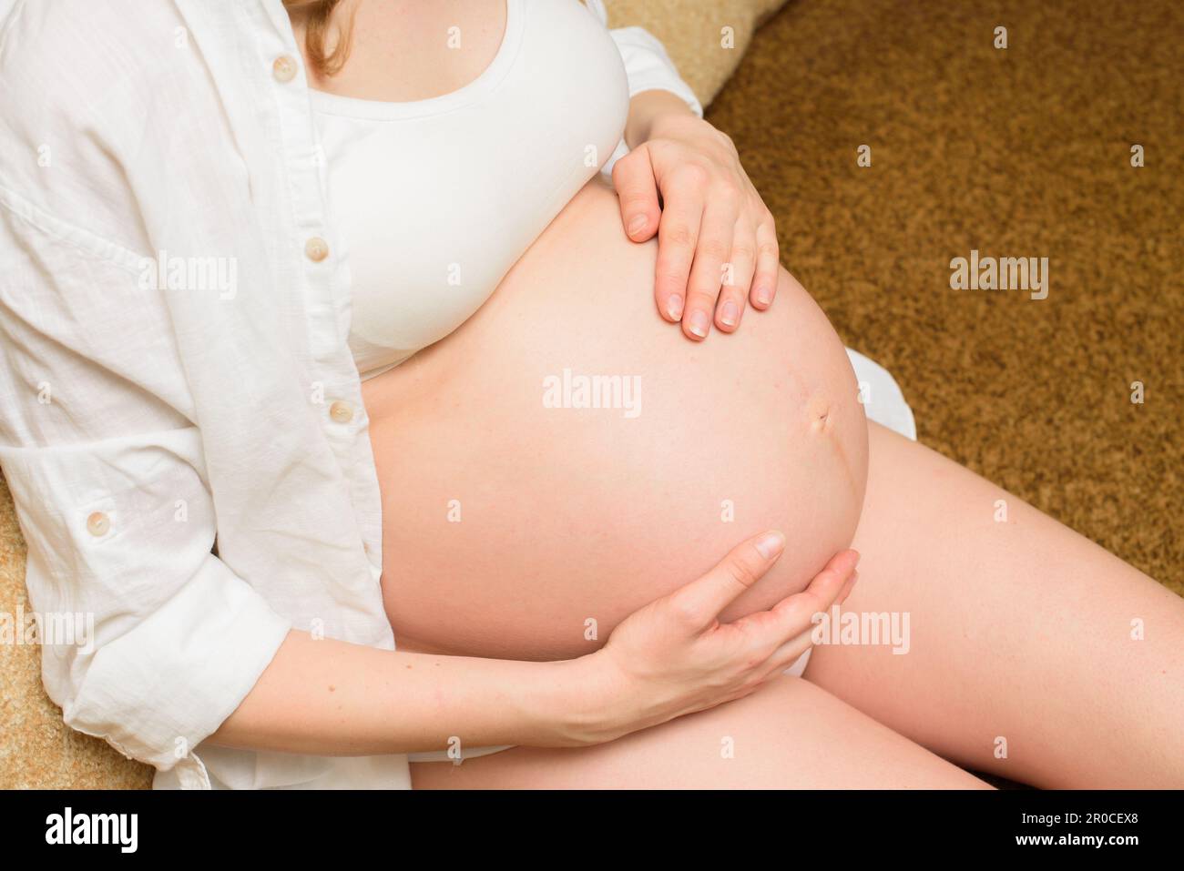 Ragazza incinta che le accarezzava il ventre, seduta sul divano. Donna incinta tenere il ventre in mano. Madre che si aspetta un bambino Foto Stock