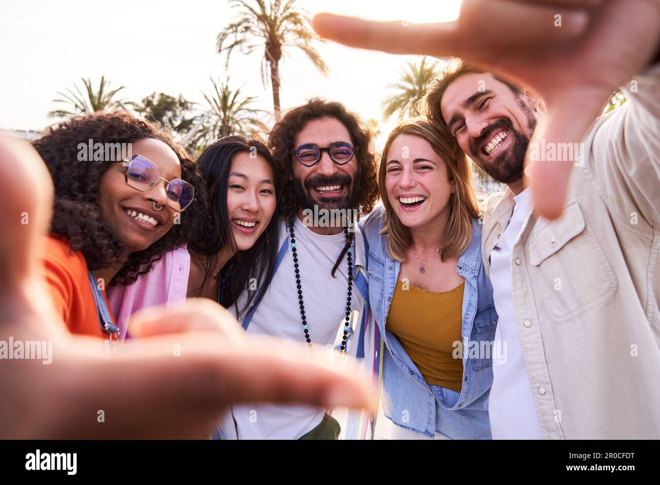 Selfie di gruppo multirrazziale di amici che fanno cornice con le dita durante le vacanze in spiaggia all'aperto. Foto Stock