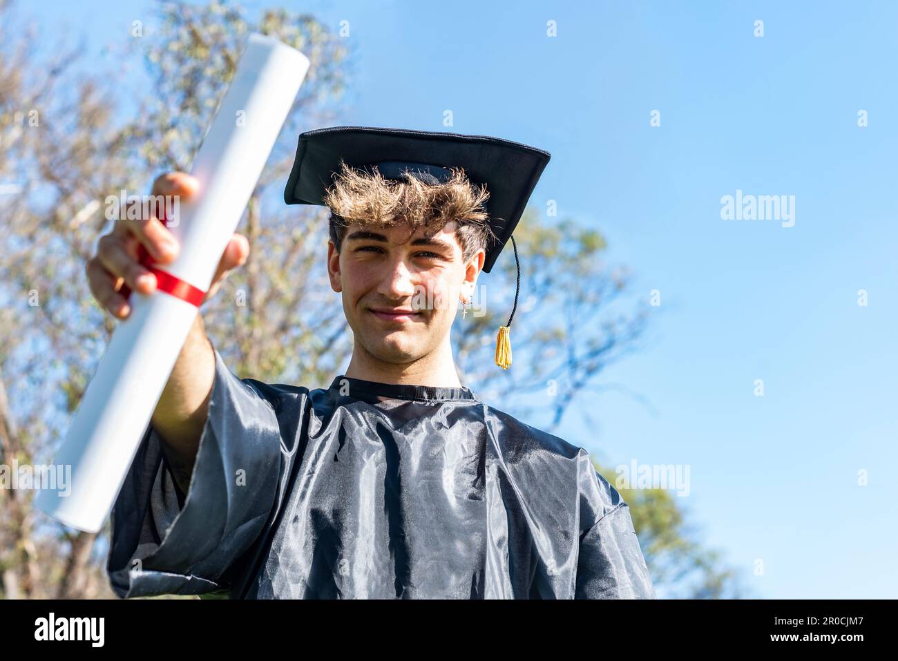 Felice giovane laureato che indossa un abito da bachelor e un mortarboard nero e che mostra il suo diploma Foto Stock