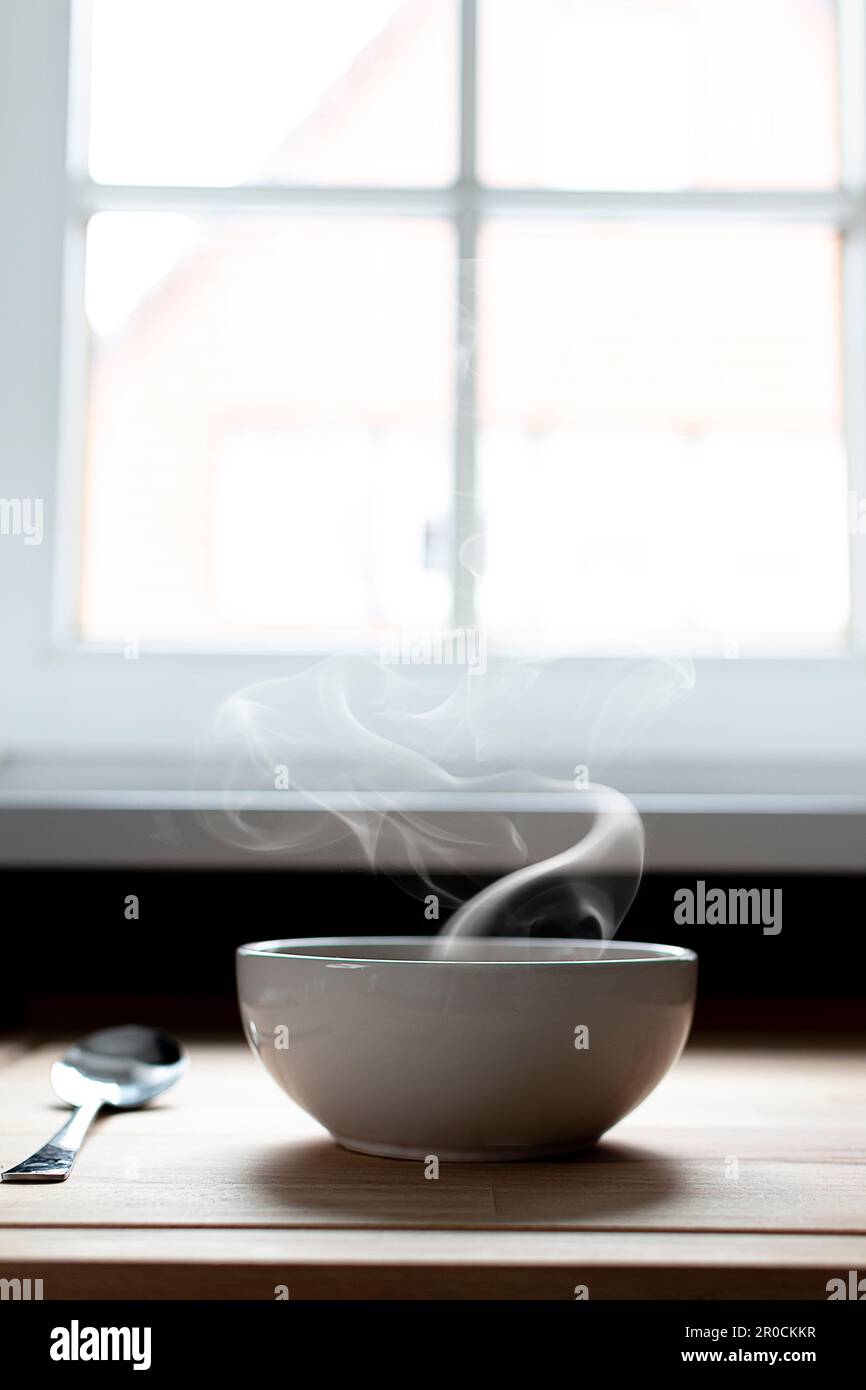 Ciotola di zuppa accanto ad una finestra. Vapore di zuppa calda. Cibo caldo Foto Stock