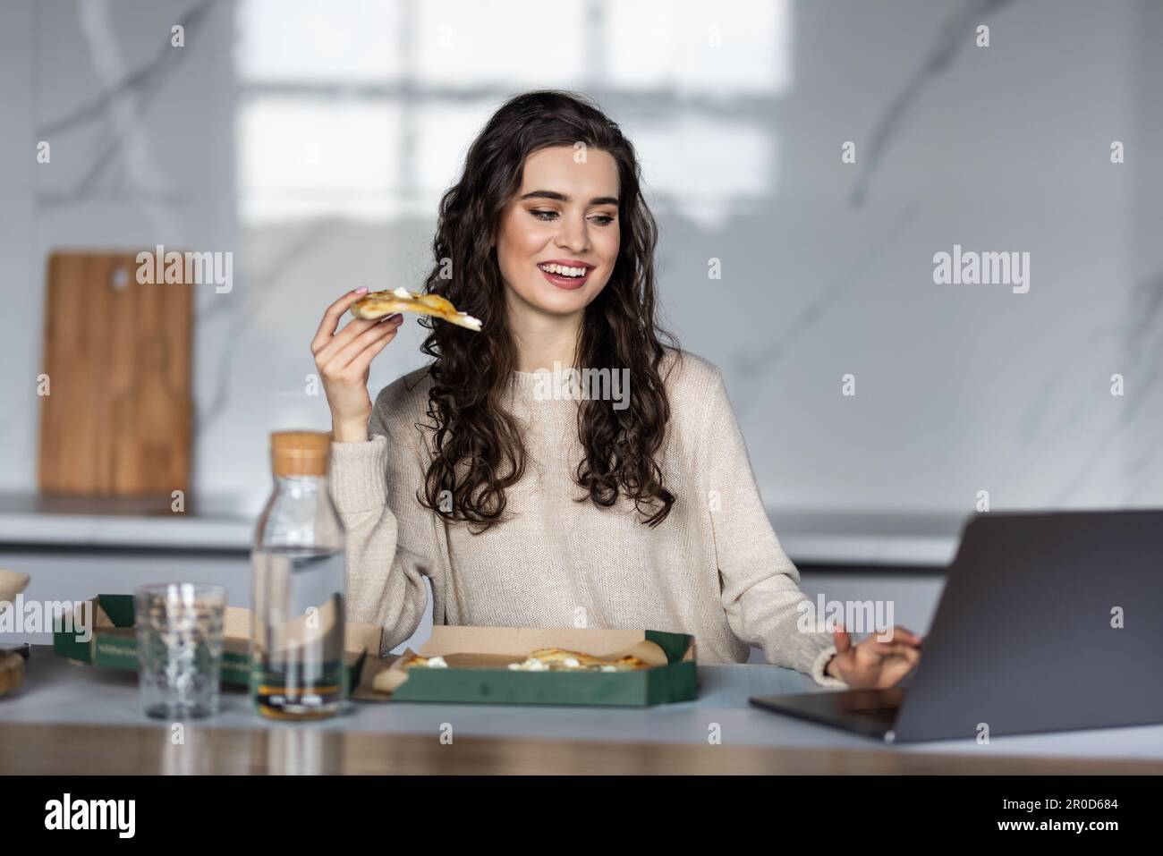 Donna overworked che prende una rottura e che mangia la pizza, lavorando da casa sul laptop Foto Stock