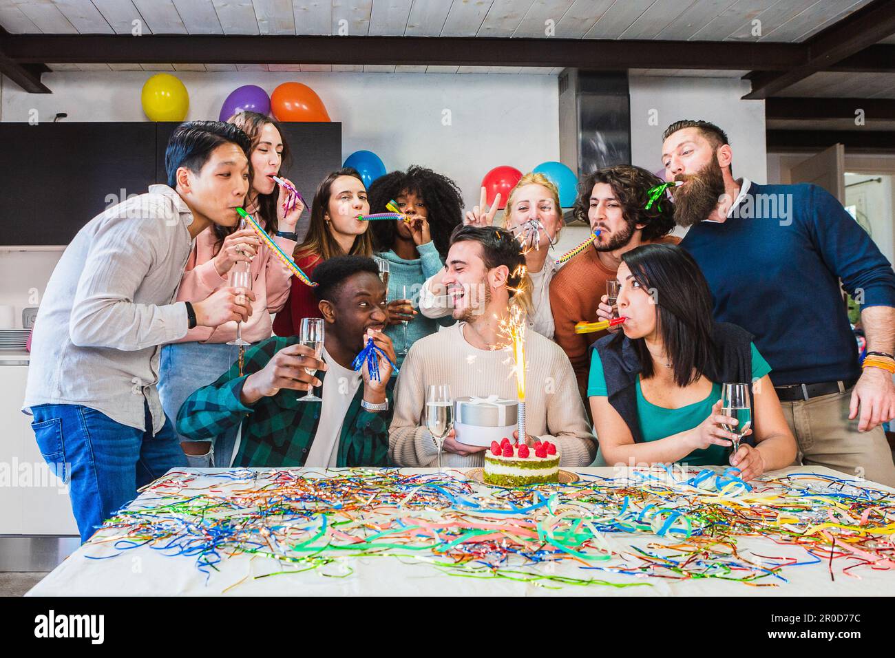 Amici felici che celebrano il compleanno del ragazzo, torta con candela fuochi d'artificio, umore festivo e risate nel salotto del ragazzo di compleanno. Filtro luminoso Foto Stock