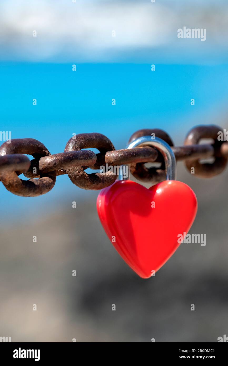 Un unico rosso, non marcato, a forma di cuore, lucchetto d'amore o lucchetto d'amore attaccato ad una fitta catena da innamorati per simboleggiare il loro affetto o amore Foto Stock