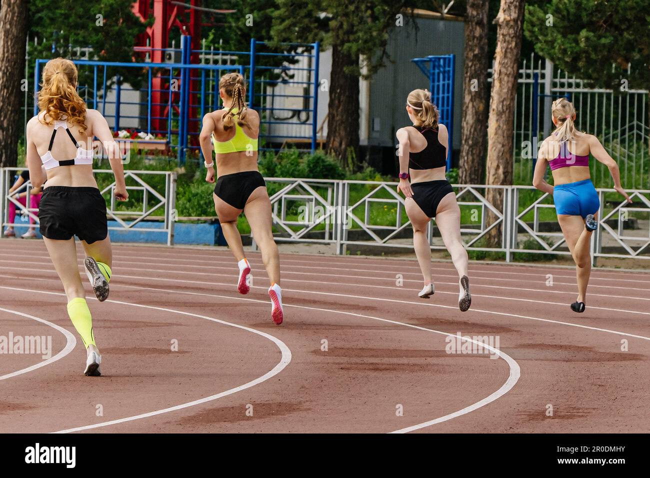 vista posteriore quattro atlete runner che corrono in sprint nei campionati estivi di atletica Foto Stock