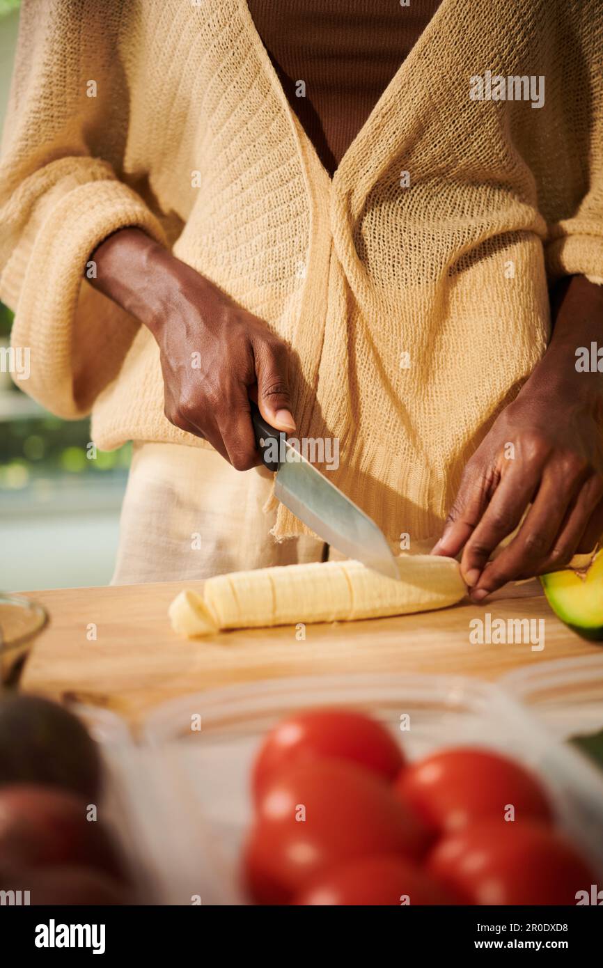 Donna che taglia la banana da aggiungere in porridge o muesli ciotola Foto Stock