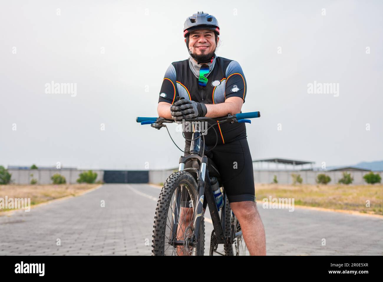 Ciclista sorridente sulla sua moto in abbigliamento sportivo. Chubby ciclista maschile in abbigliamento sportivo a cavallo di una bicicletta all'aperto Foto Stock