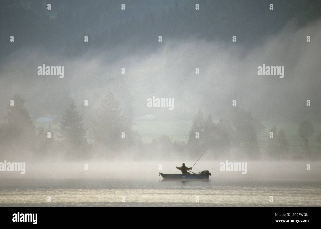 Pescatore in barca sul lago Kochelsee nella nebbia mattutina, Baviera, Germania Foto Stock