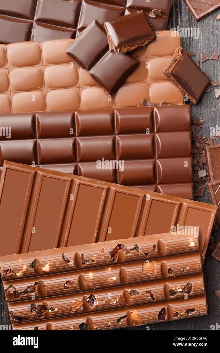 Nero, latte, cioccolato aerato, cioccolato con noci e uva passa su uno sfondo di legno scuro vista dall'alto. Sfondo cioccolato. Foto Stock