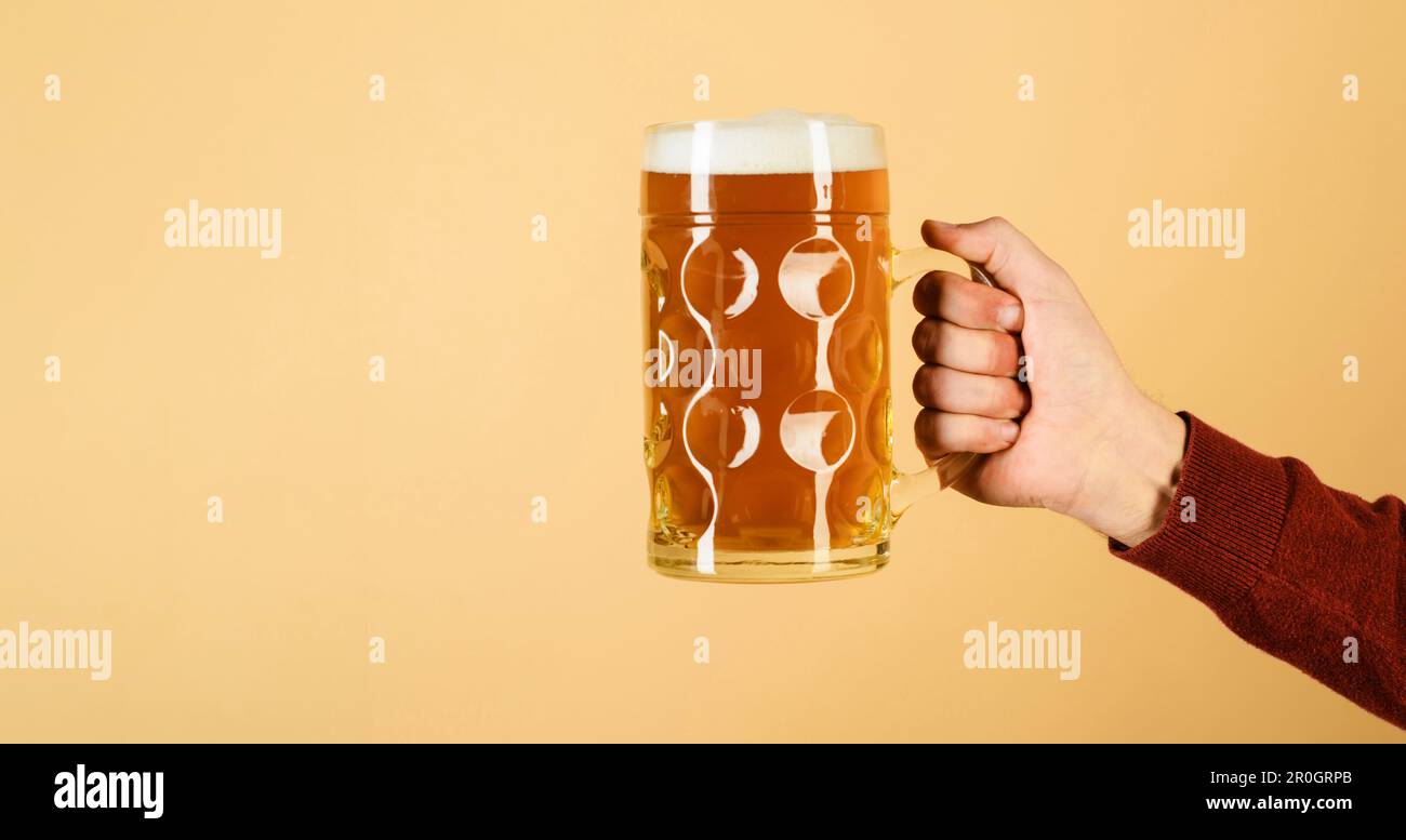 Oktoberfest festival. Mano dell'uomo che tiene tazza di birra più lager. Bar o pub. Birra fresca fredda con schiuma spessa. Mano maschio con bicchiere di birra. Birra bavarese. Mano Foto Stock