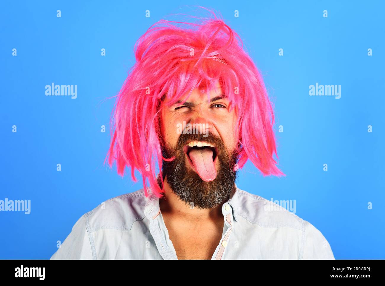 Uomo bearded divertente in parrucca rosa mostra lingua. Inocchiare l'uomo con barba e baffi in parrucca. Espressione del volto. Sensazioni ed emozioni. Hippster in periwig Foto Stock