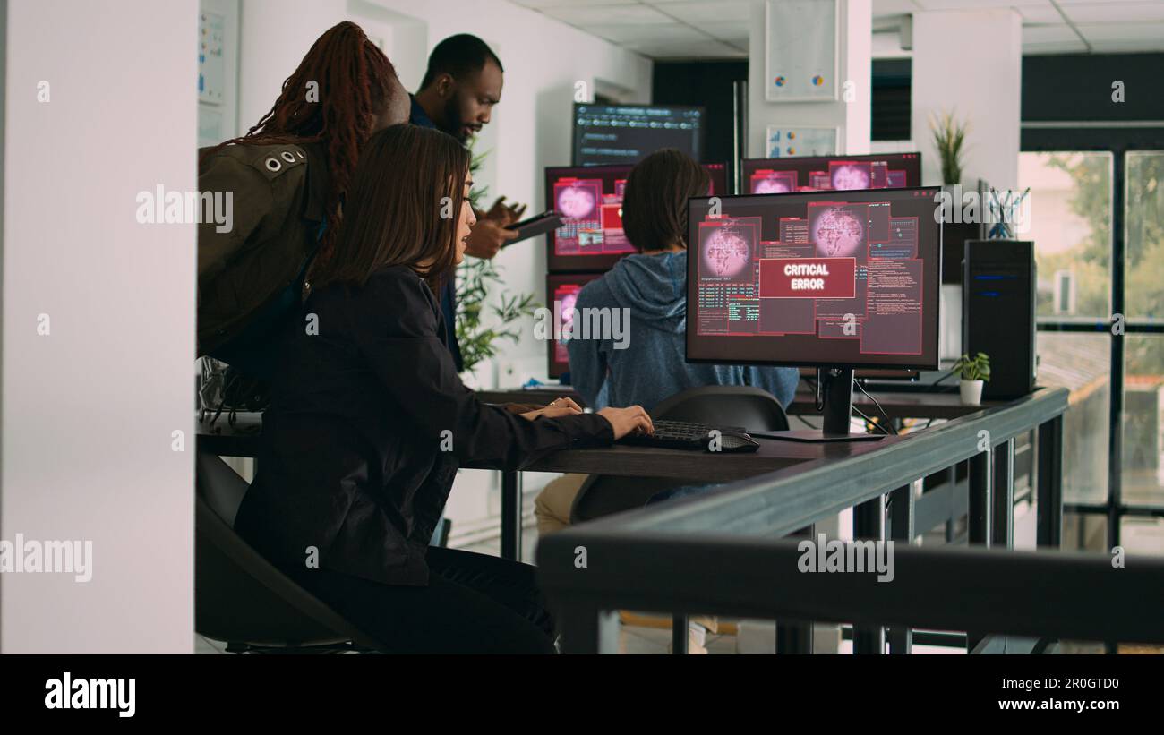 Gruppo multietnico di sviluppatori di applicazioni che leggono errori critici su più monitor nell'agenzia IT, violati. Lavorare con il codice di intelligenza artificiale e il database dei server per fermare l'hacking del programma. Foto Stock