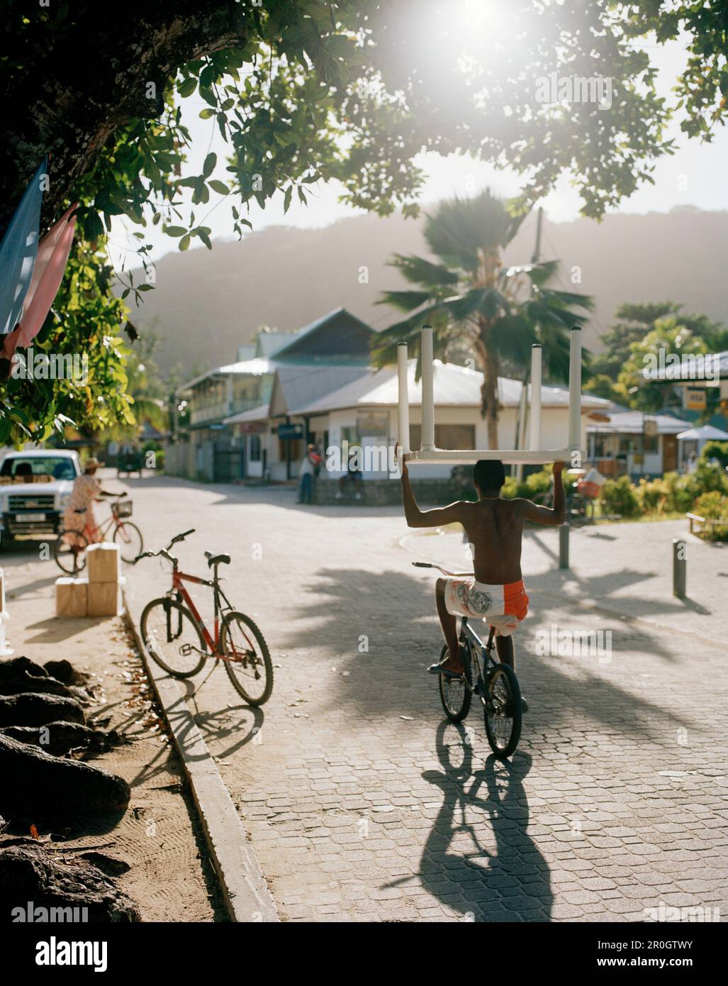 Biker che porta un tavolo di plastica sulla sua testa sulla strada principale al mattino, la Passe, la Digue e Inner Islands, Repubblica delle Seychelles, Oceano Indiano Foto Stock