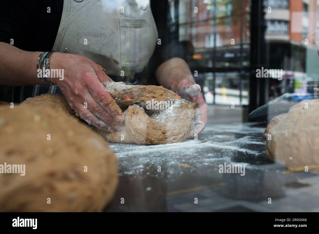 Primo piano delle mani di lavoro in una panetteria dietro una finestra di vetro Foto Stock