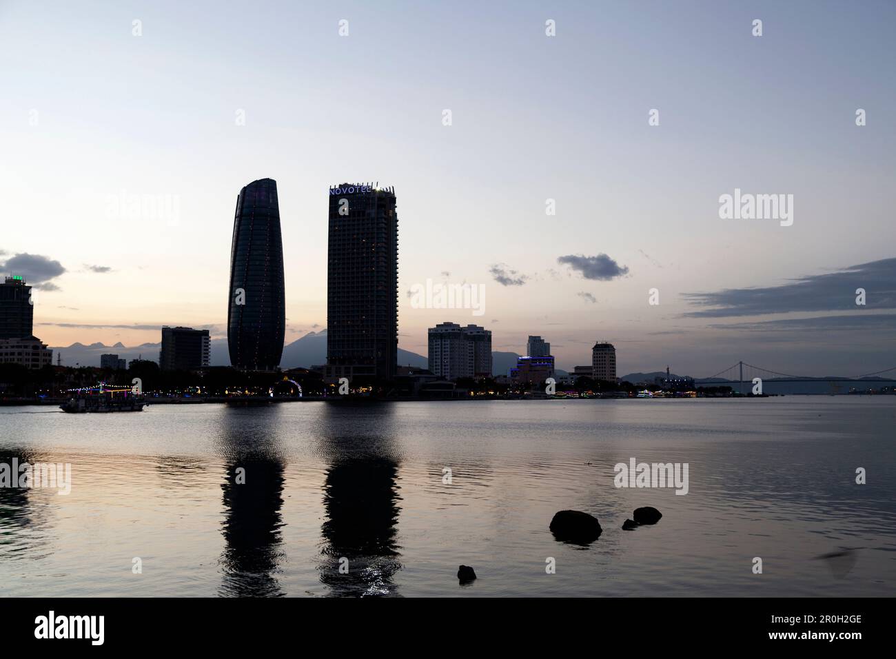 Da Nang, Vietnam - 20 2018 agosto: Battello che passa davanti al centro amministrativo della città di da Nang e al Novotel sul fiume Han al tramonto. Foto Stock