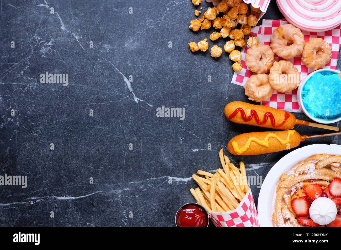 Bordo lato cibo a tema carnevale su uno sfondo scuro. Vista superiore con spazio di copia. Concetto di fiera estiva. Cani da granoturco, torta a imbuto e spuntini. Foto Stock