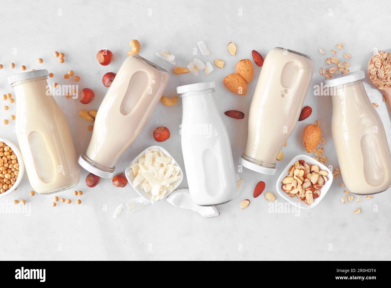 Latte vegano, a base di piante, non latticini. Varietà di bottiglie di latte con ingredienti sparsi. Vista dall'alto su uno sfondo di marmo bianco. Foto Stock