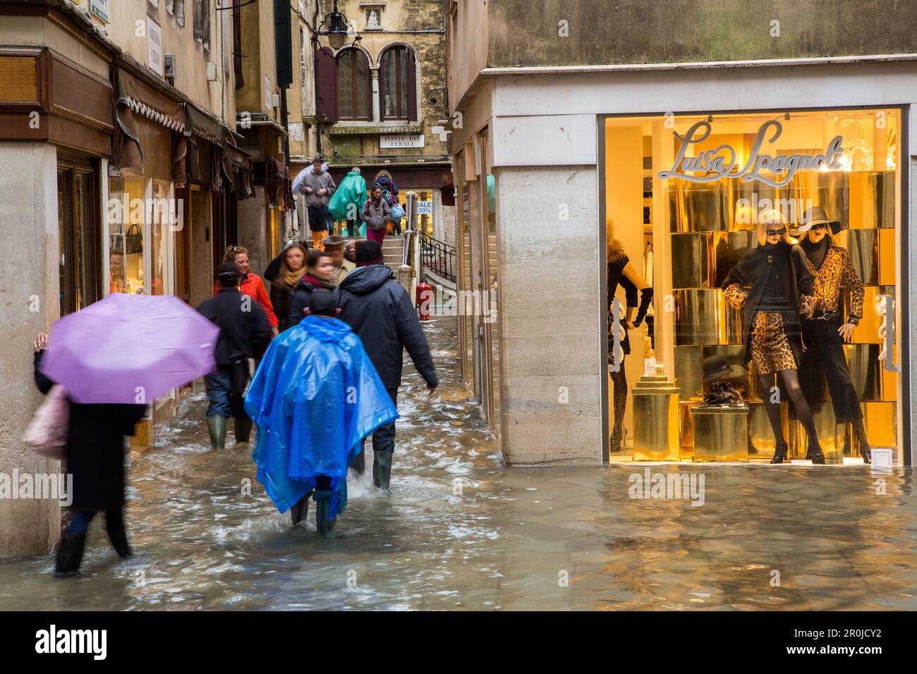 Turisti con ombrelloni e scarpe coperte in plastica, stivali in gomma,  acqua alta, negozio di moda vicino a Piazza San Marco, acqua alta causata  da si Foto stock - Alamy