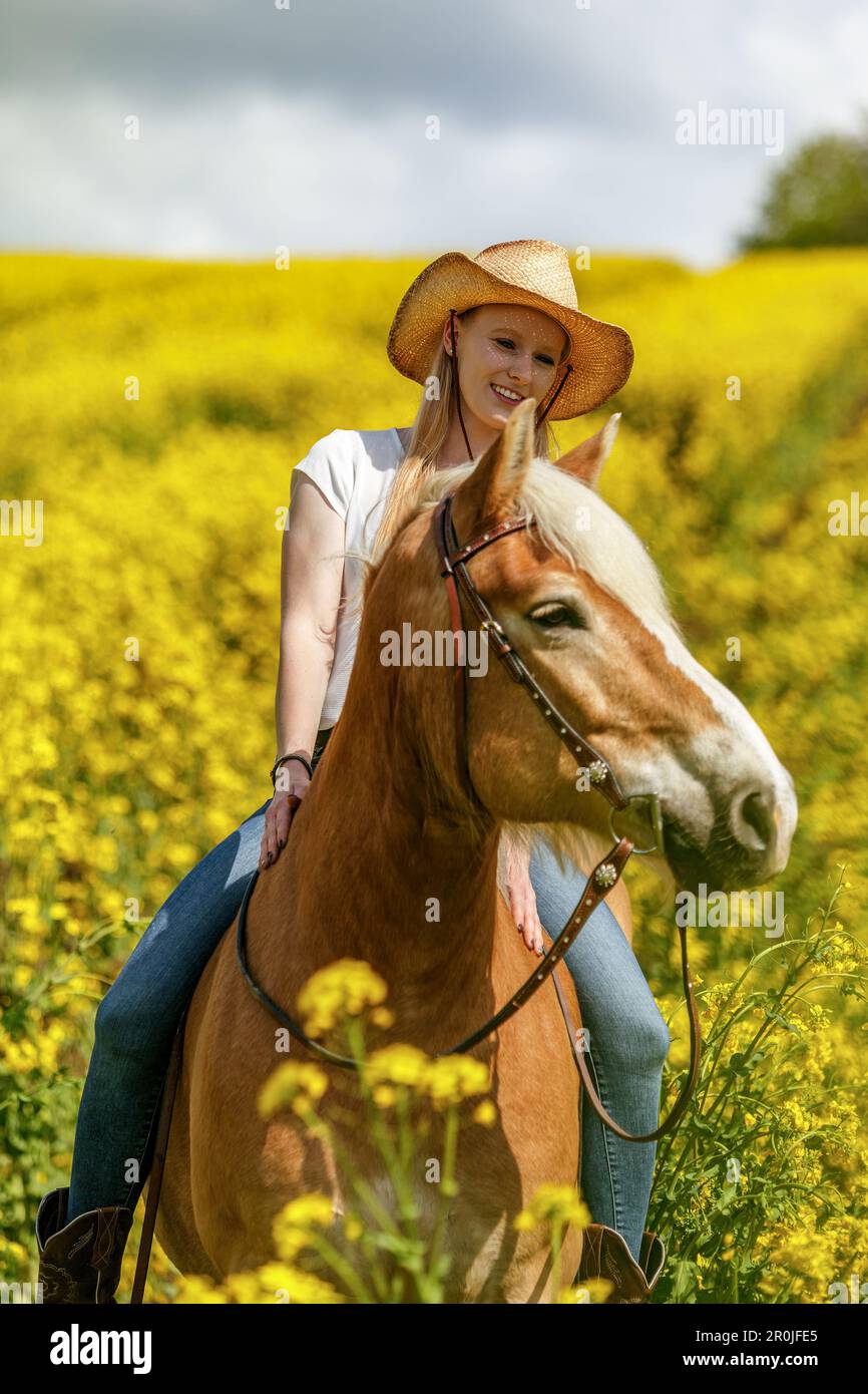 Una giovane donna bionda e il suo cavallo haflinger che si divertono in primavera all'aperto. Scena di amicizia tra una donna equestre e il suo pony Foto Stock