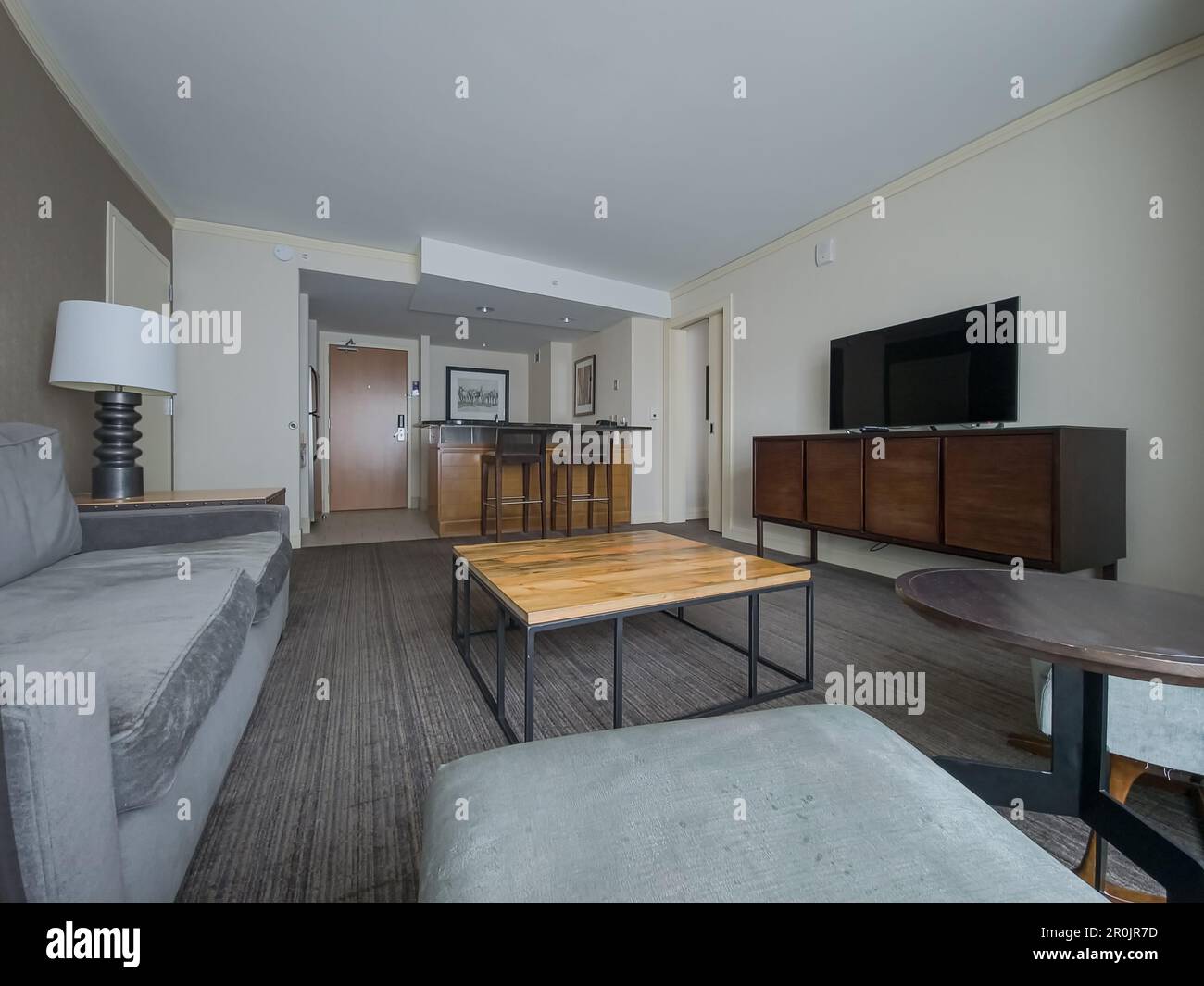 Suite business vuota con tv a schermo piatto, divano, tavolo in legno, sgabelli da bar Foto Stock