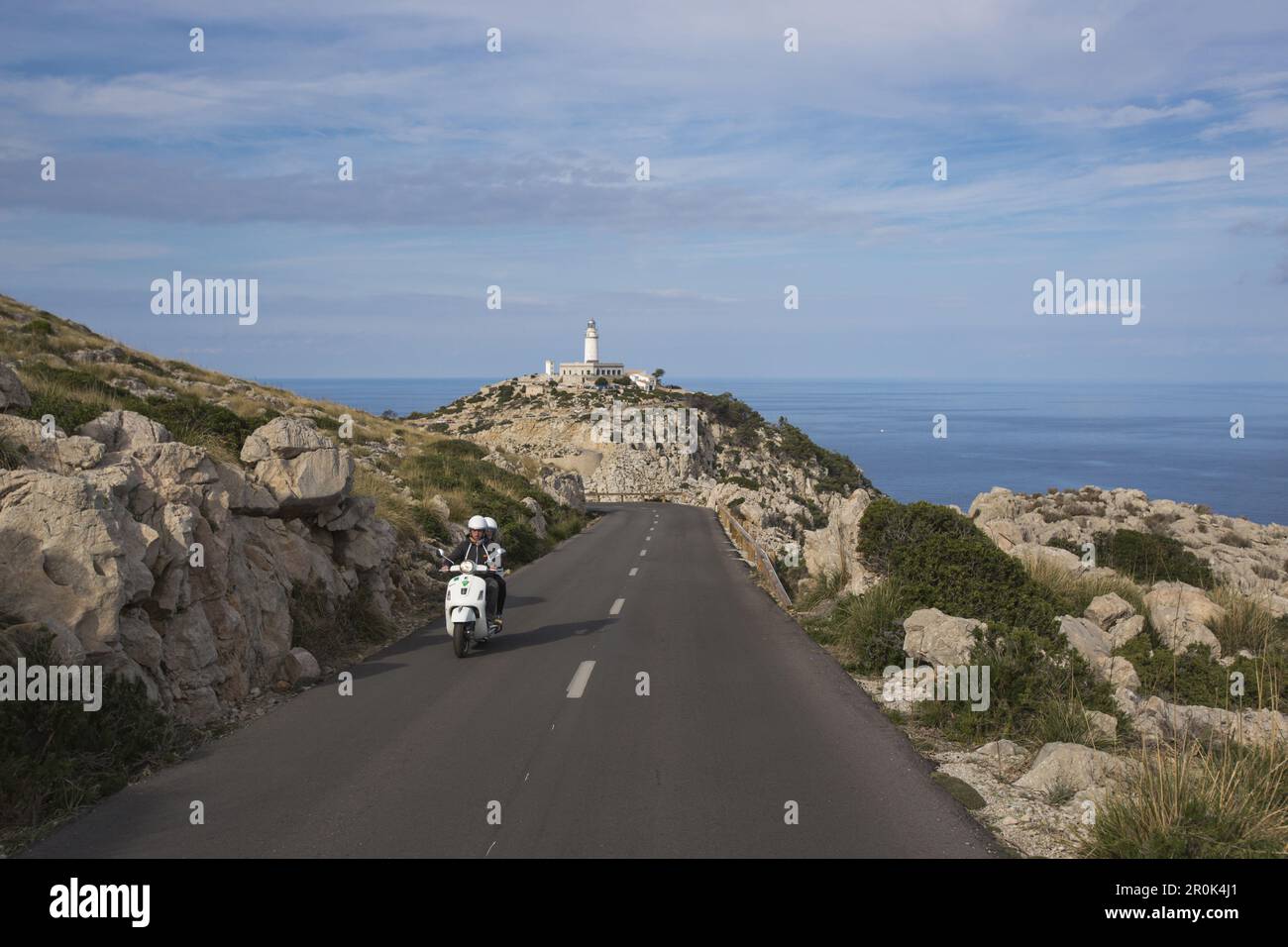 Coppia su scooter bianco su strada lungo la penisola di Cap de Formentor con faro di Faro de Formentor dietro, Cap de Formentor, Maiorca, Isole Baleari Foto Stock