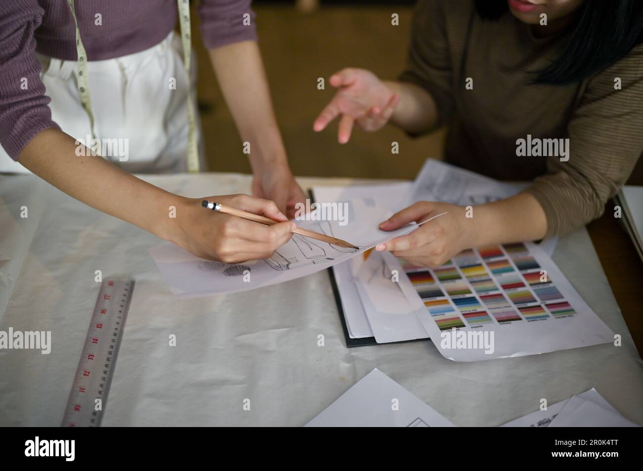 Due stilisti di moda o comò professionisti che discutono e controllano insieme i nuovi schizzi di modelli in studio. immagine ritagliata Foto Stock