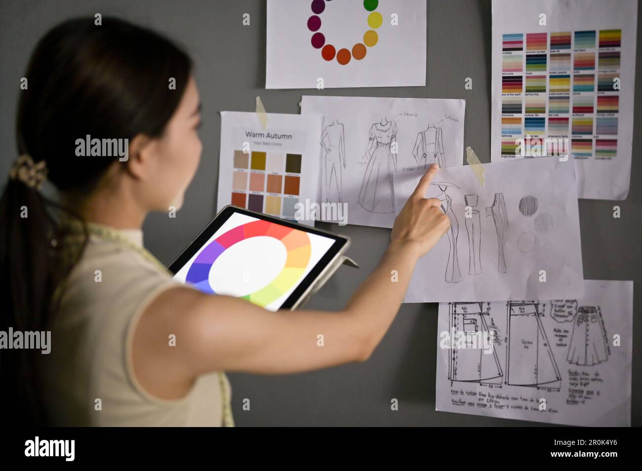 Designer di moda femminile asiatica professionale e creativa con il suo tablet digitale che controlla la nuova collezione di schizzi design nel suo studio. vista posteriore Foto Stock