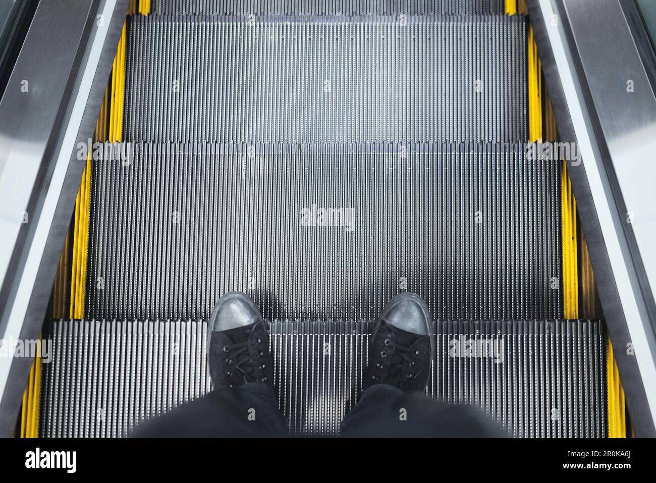 Vista dall'alto delle gambe delle sneakers in piedi sul gradino della scala mobile Foto Stock