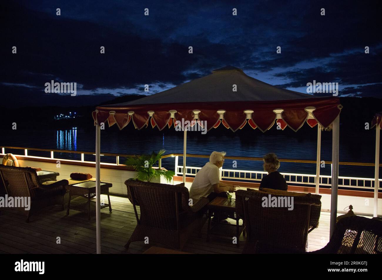 Gli ospiti si rilassano sotto la baldacchino sul ponte di Ayeyarwady (Irrawaddy) nave da crociera sul fiume Anawrahta (linea Heritage) di notte, vicino a Ngayiphyo, Sagaing, Myanmar Foto Stock