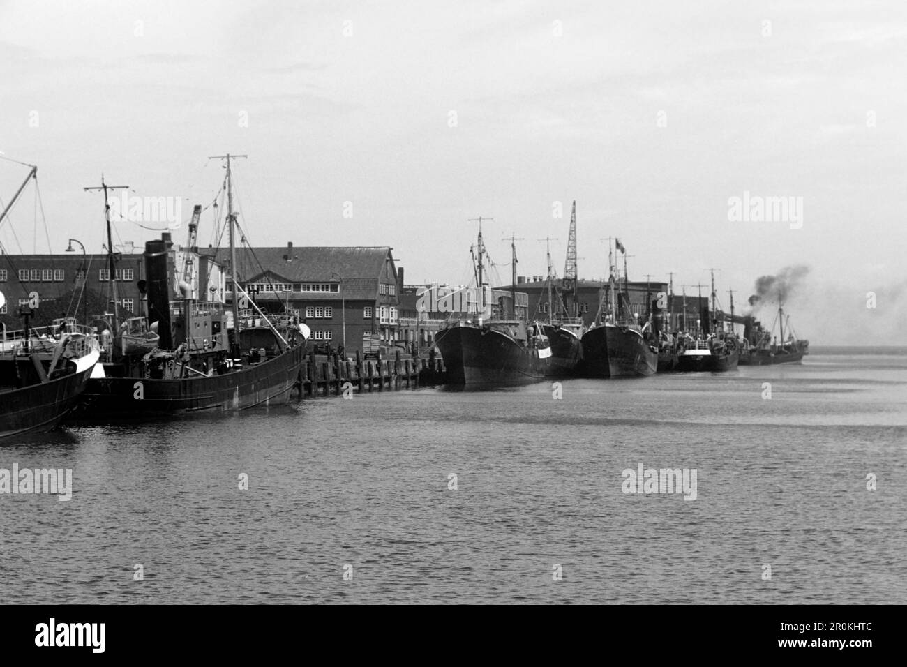 Fichtutter im Fischereihafen Cuxhaven, das Verwaltungsgebäude und die alte Netzhalle im Hintergrund, 1960. Pescatore nel porto di pesca di Cuxhaven, l'edificio amministrativo e il vecchio salone delle reti sullo sfondo, 1960. Foto Stock
