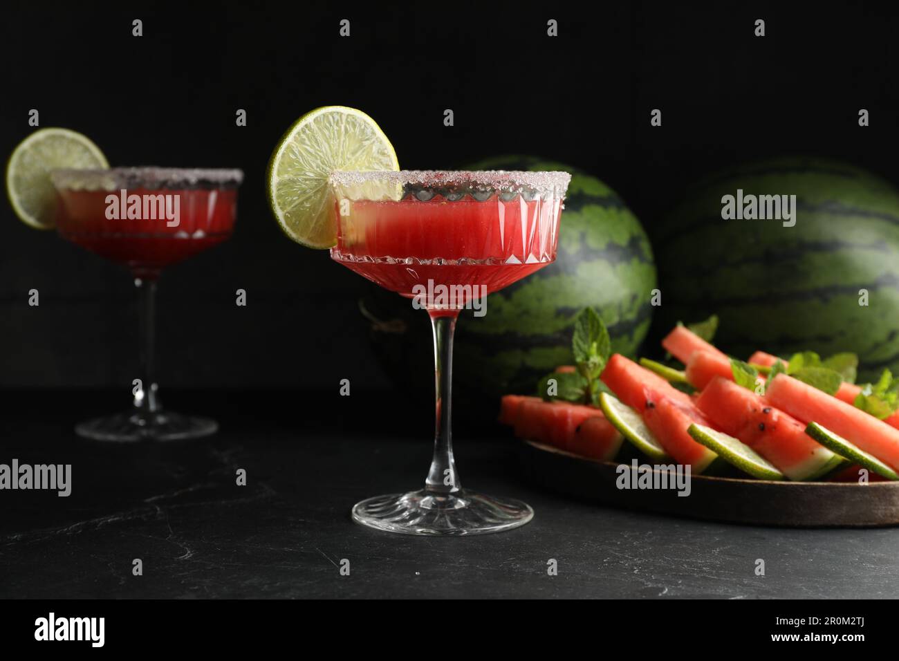 Bicchieri da cocktail di delizioso succo di cocomero fresco con lime e zucchero sul tavolo nero Foto Stock