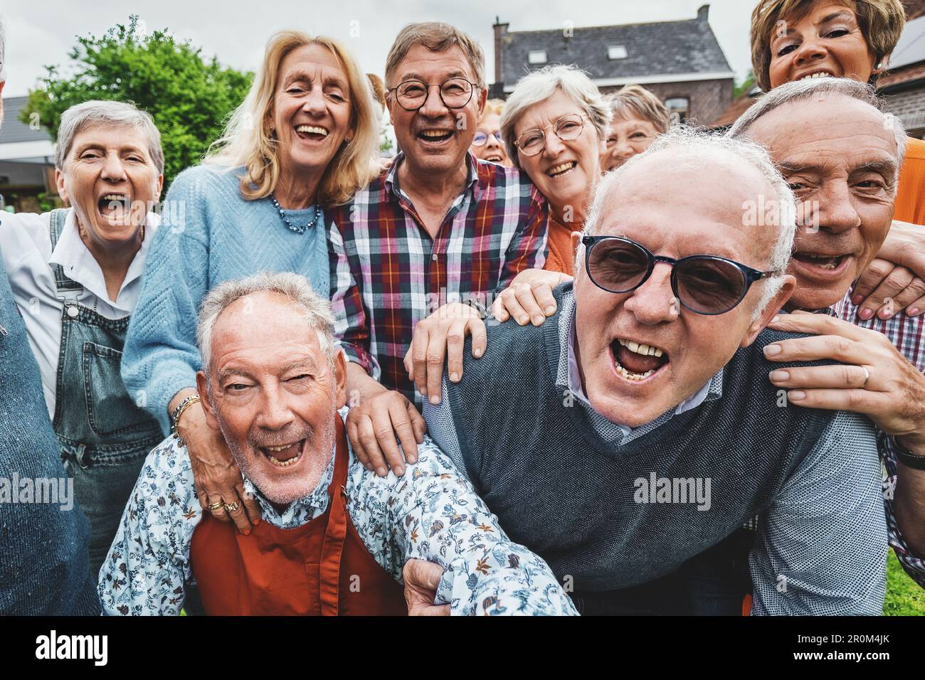 Un vivace gruppo di oltre 65 amici si è riunito in una casa di campagna, ridendo e gridando insieme mentre prendono un selfie di gruppo gioioso. Foto Stock