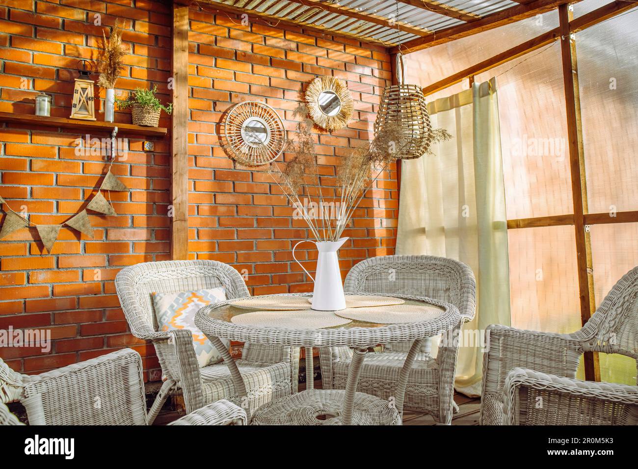 Terrazza con patio in stile boho con tende e decorazioni in vimini, rattan e canna. Parete in plastica serra e soffitto in policarbonato. Foto Stock