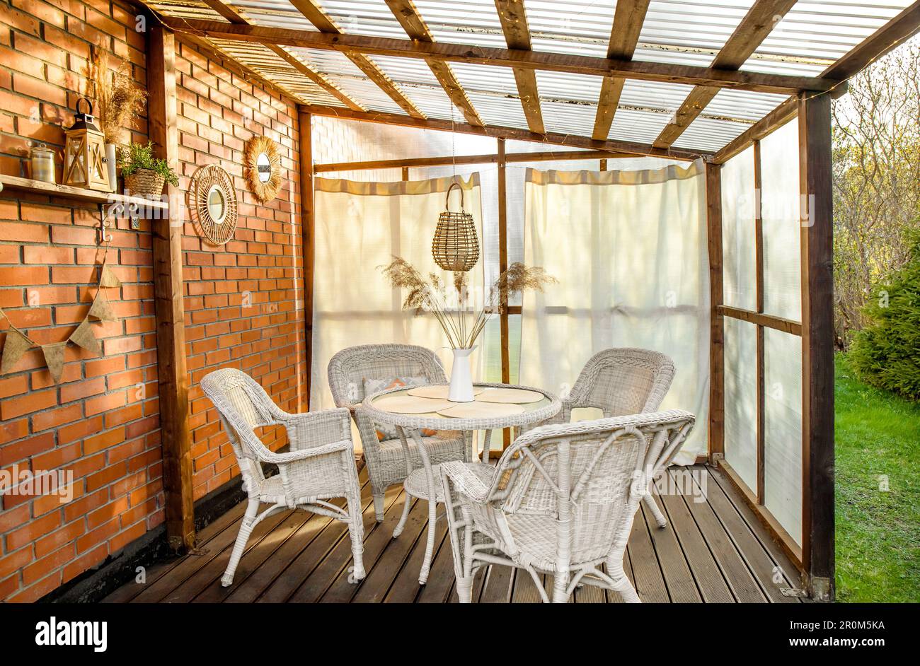 Terrazza con patio in stile boho con tende e decorazioni in vimini, rattan e canna. Parete in plastica serra e soffitto in policarbonato. Foto Stock