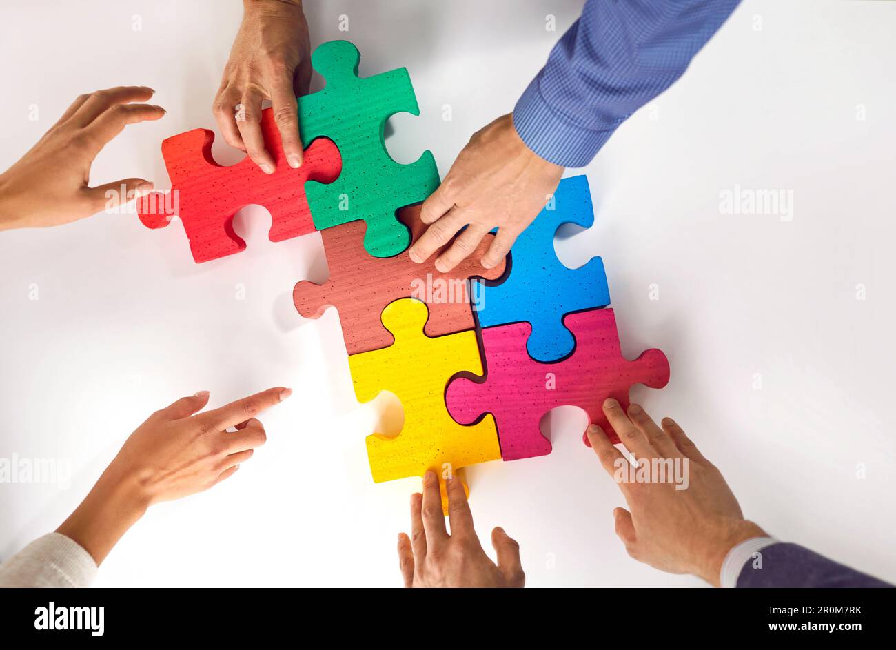 Gruppo di tre giovani mettere puzzle colorati sul tavolo e presentare il concetto di cooperazione, lavoro di squadra, sostegno e assistenza in ufficio. Foto Stock