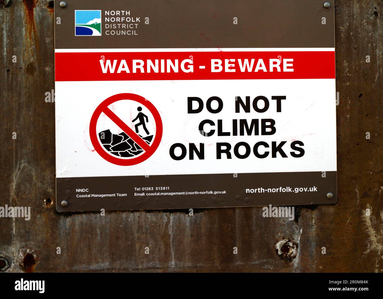 Un cartello di avvertimento sul lungomare per non salire sulle rocce di difesa del mare per motivi di sicurezza sulla costa nord del Norfolk a Sheringham, Norfolk, Inghilterra, Regno Unito. Foto Stock