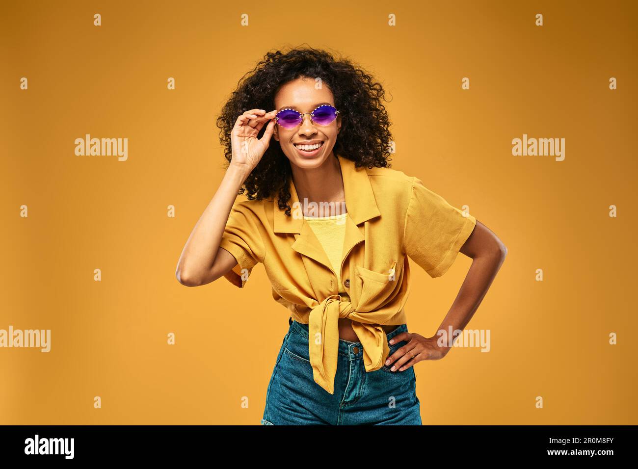 Ritratto estivo di giovane donna alla moda che indossa abiti alla moda e occhiali da sole in piedi su sfondo giallo in studio Foto Stock
