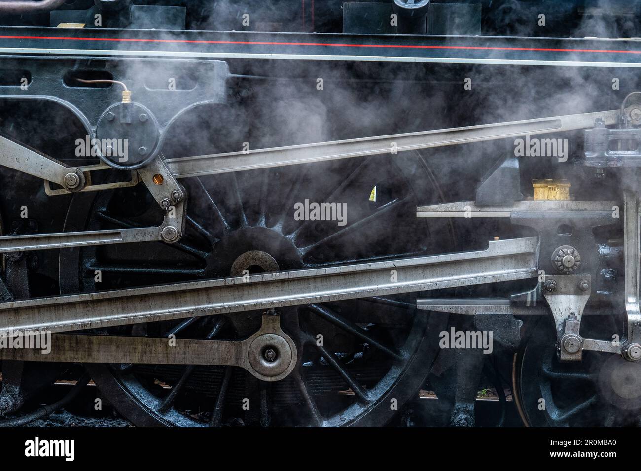 Un motore a locomotiva a vapore nero che emette fumi bianchi sullo sfondo di tubi in acciaio Foto Stock
