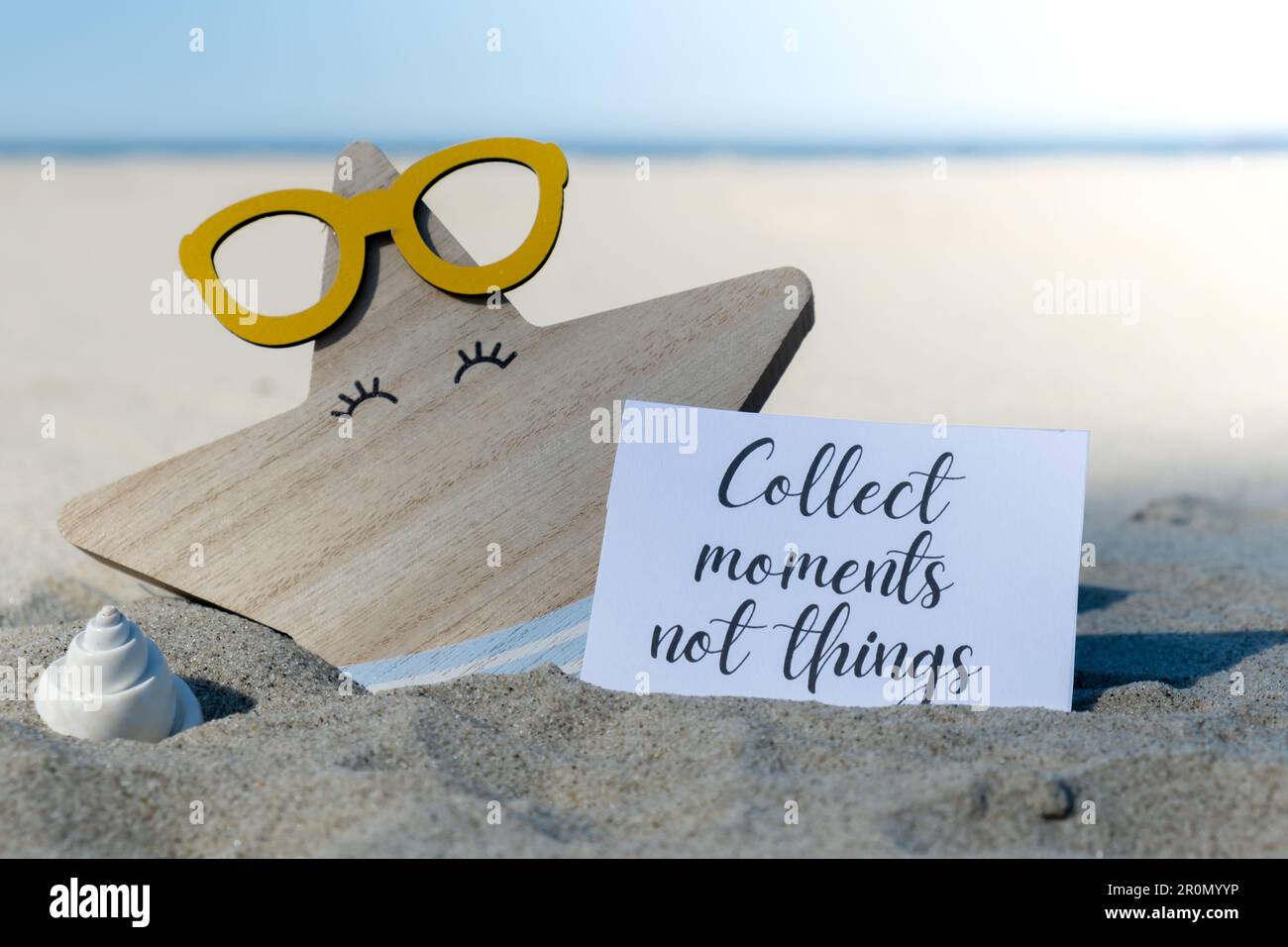 RACCOGLIERE MOMENTI NON COSE testo su carta biglietto di auguri sullo sfondo di divertente stella marina in occhiali decorazione vacanza estate. Spiaggia di sabbia costa sole. Rallentare, godersi il momento, momenti buoni, slow life concetto di vacanza cartolina. Un concetto di viaggio d'affari Foto Stock