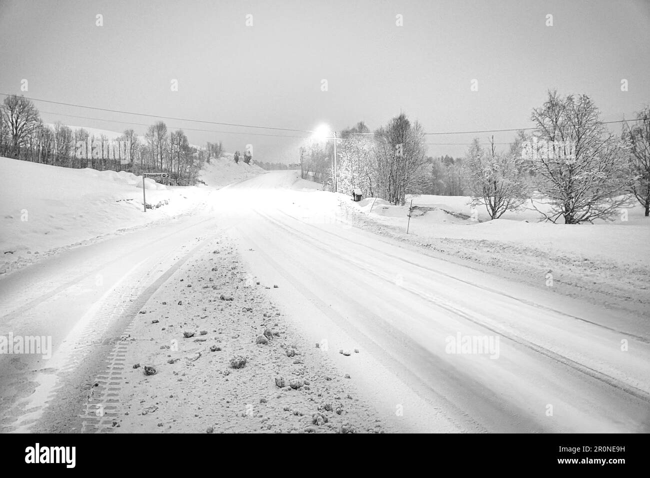 Paesaggio invernale in Scandinavia in bianco e nero. Strada innevata con alberi innevati. Sulla strada brilla un lampione. Foto di paesaggio dal NOR Foto Stock