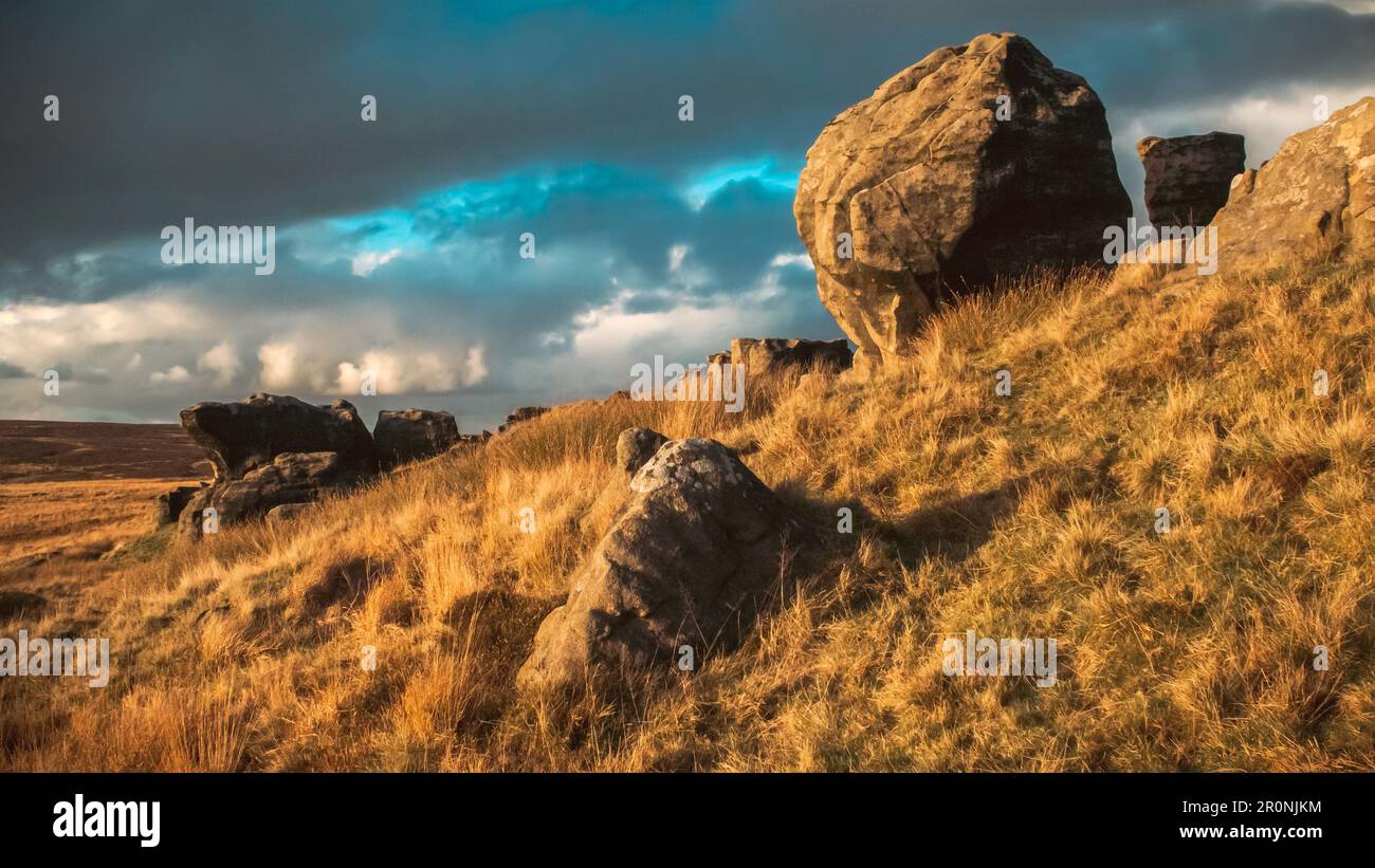 Ampia fotografia paesaggistica di grandi rocce lavate in luce dorata su una collina contro un cielo nuvoloso al tramonto Foto Stock