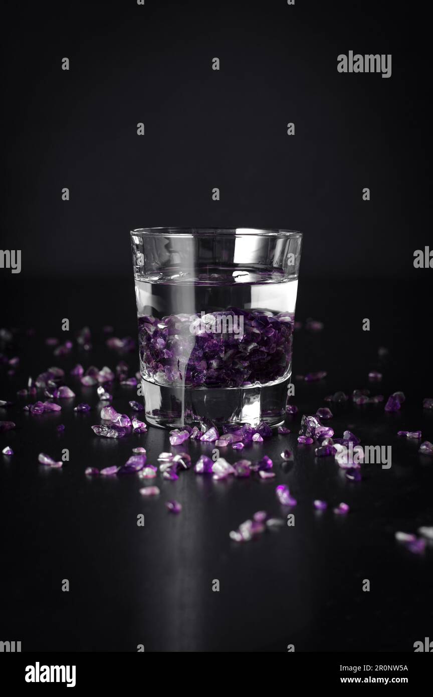 patatine ametista in un bicchiere d'acqua con fondo nero. gemma di guarigione, strega moder Foto Stock