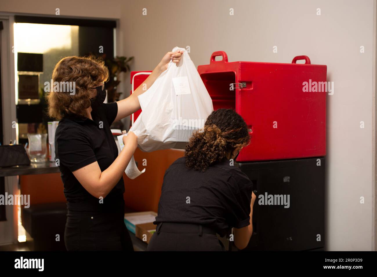 Los Angeles, California, Stati Uniti - 08-24-2021: Una visione di due dipendenti femminili che gestiscono ordini di cibo da andare in entrata e in uscita da un armadietto alimentare. Foto Stock
