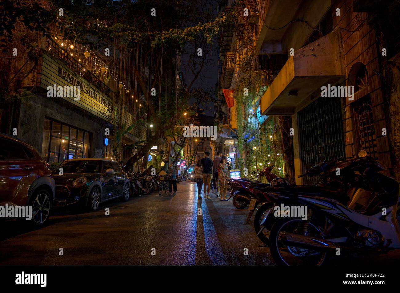 Vita di strada nel vecchio quartiere di Hanoi dopo il tramonto con la popolare Pasteur Street Brewing Co. Toccare la camera a sinistra e la strada drappeggiata in lianas. Vietnam. Foto Stock