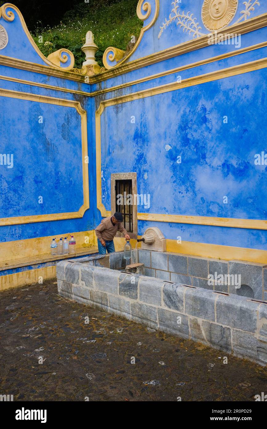 Un uomo locale che riempie bottiglie d'acqua di plastica alla Fontana Sabuga di Sintra Foto Stock
