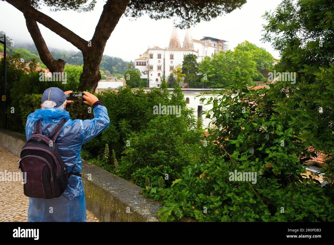 Un turista che indossa una copertura impermeabile in plastica scatta una foto del Palazzo Nazionale di Sintra in una giornata di pioggia Foto Stock