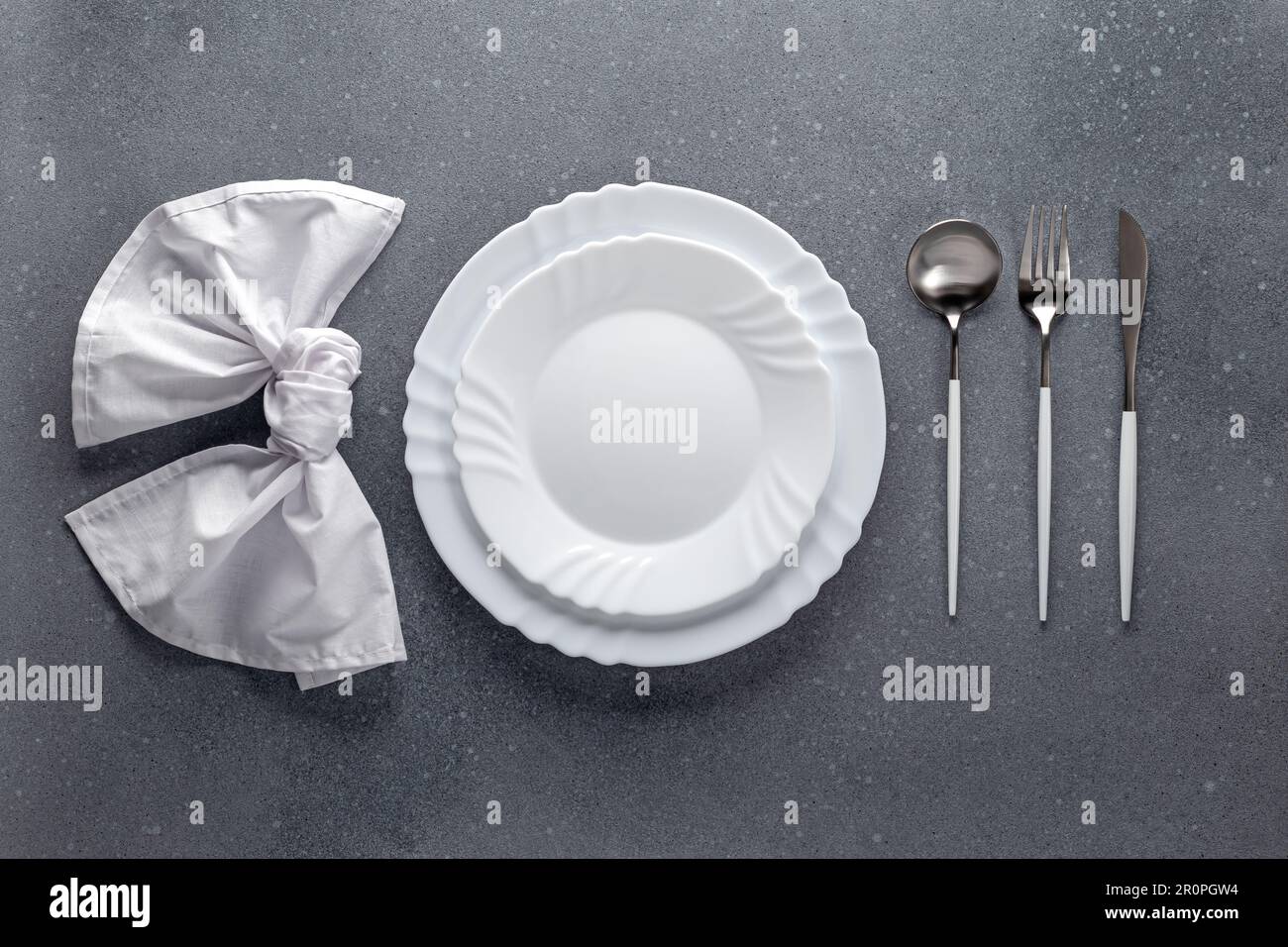 Posizionare l'impostazione con tovagliolo bianco, piatto vuoto e posate argentate su un tavolo grigio in cemento. Vista dall'alto. Cena festiva in un bar. Modello di menu, fl Foto Stock